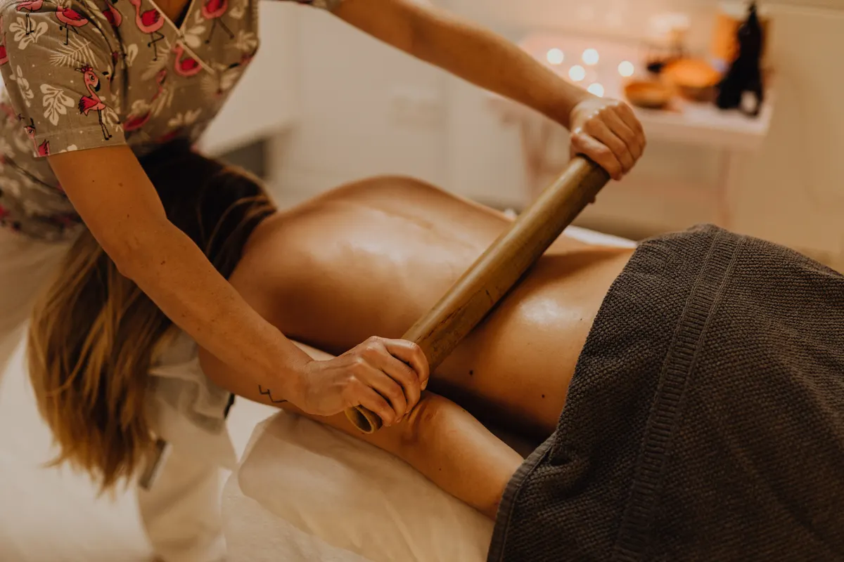 A massage therapist working along a client's back with a wooden roller in a candlelit treatment room.