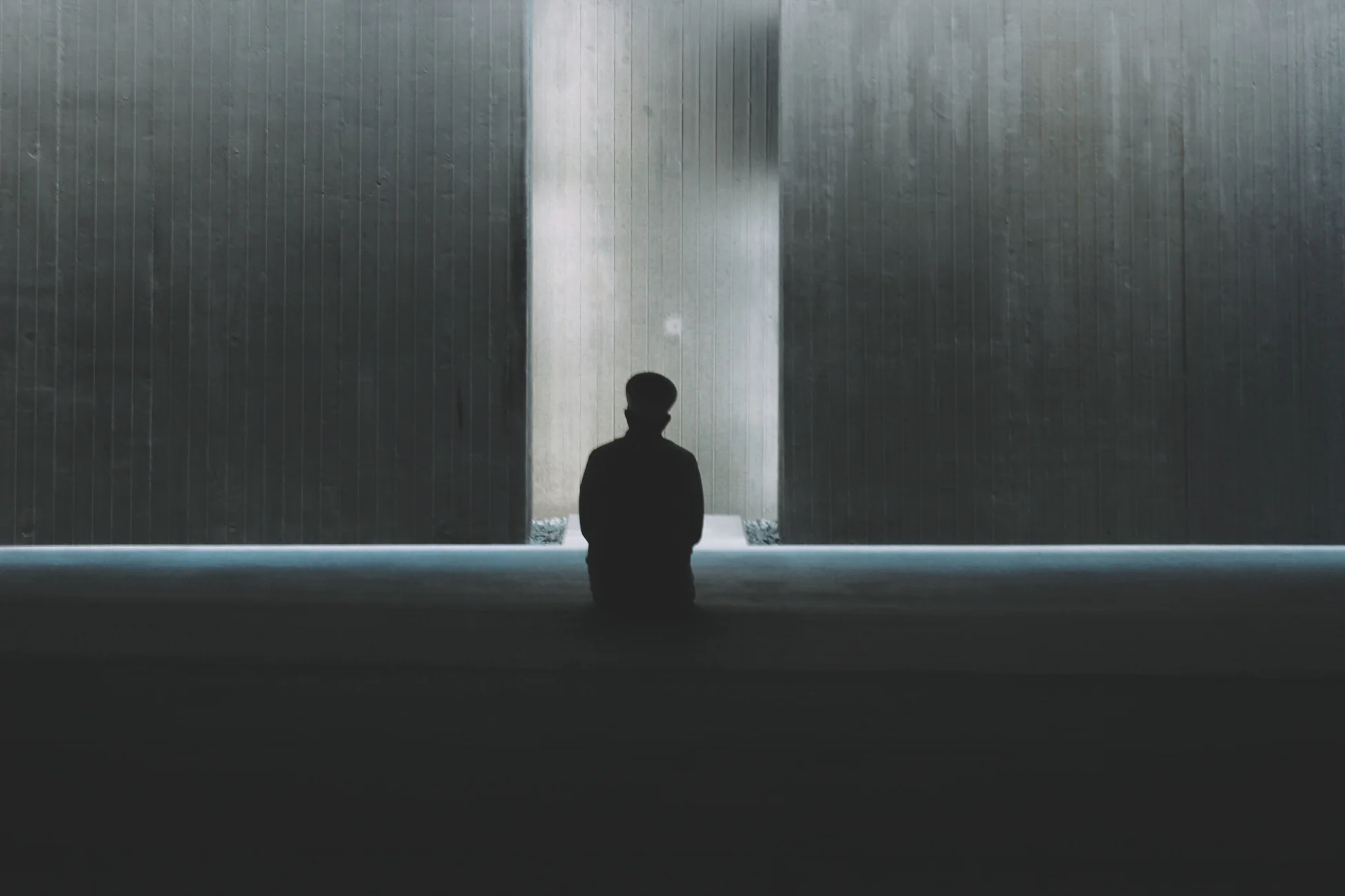 A lone figure sitting in a vast concrete hall, dwarfed by the space around them.