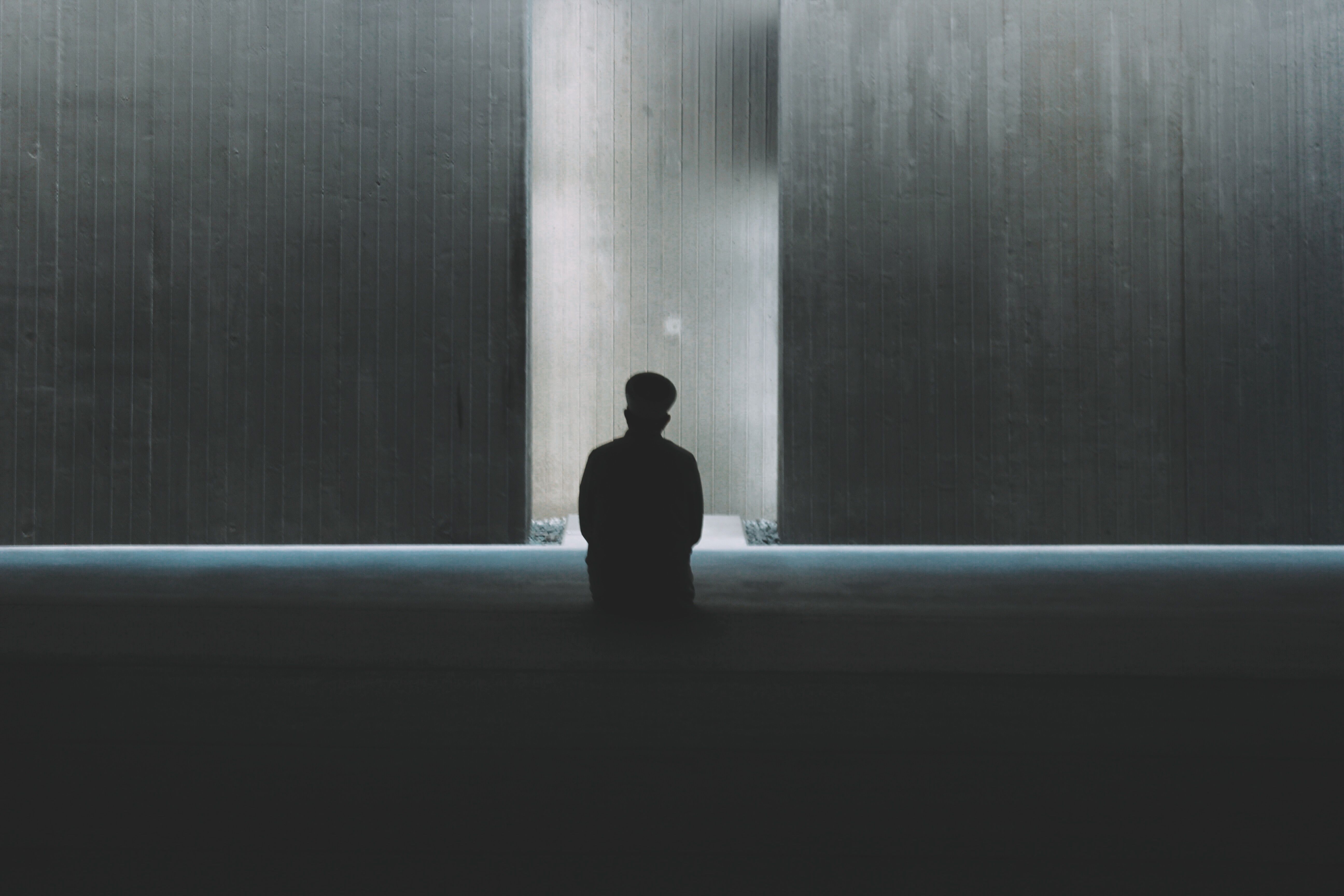A lone figure sitting in a vast concrete hall, dwarfed by the space around them.