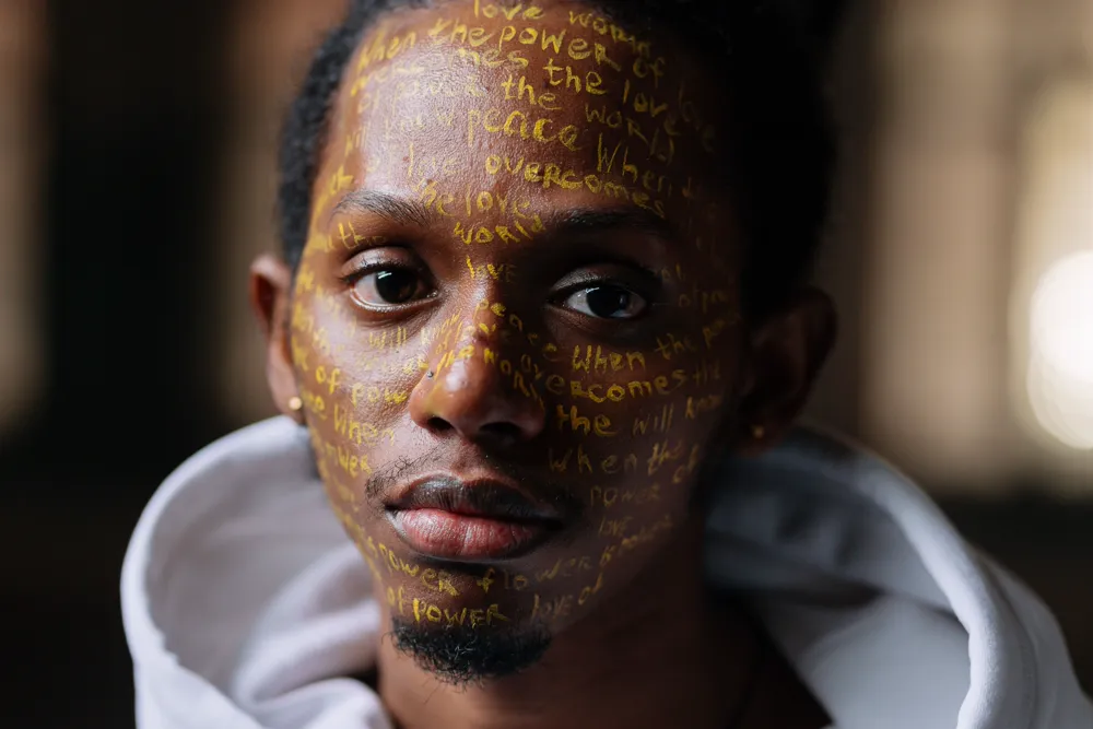 A person's face inscribed with lines of handwritten words in gold.