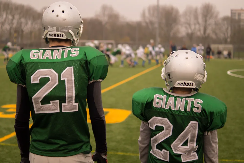 Two American football players from the back, both wearing the same GIANTS team shirt.