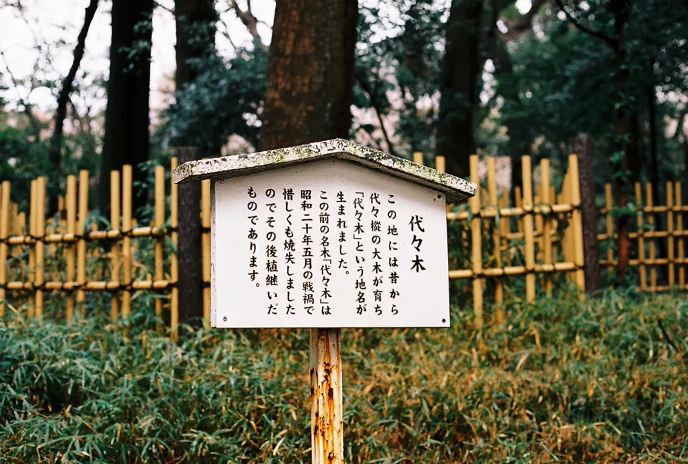 A wooden signboard in a forest explaining the origin of a Japanese place name.