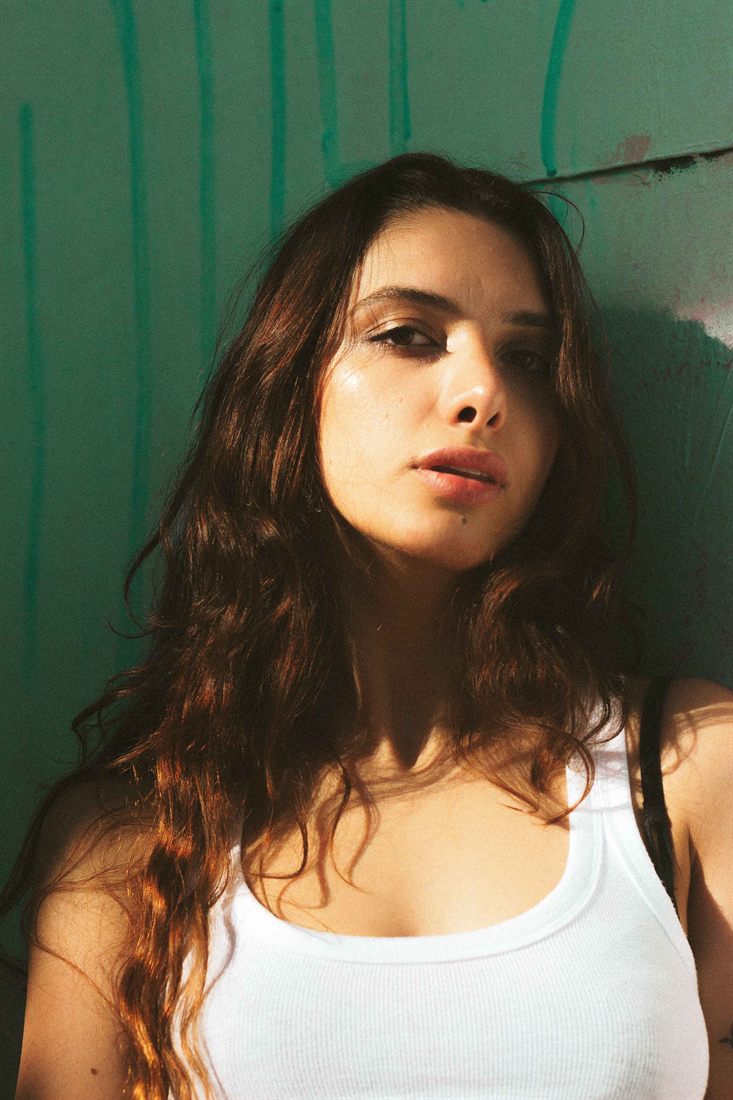 An editorial portrait lit by warm sunlight against a green wall