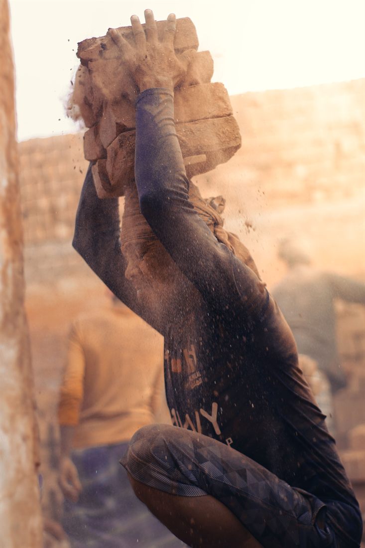 A builder lifting bricks on a construction site, dust in the air